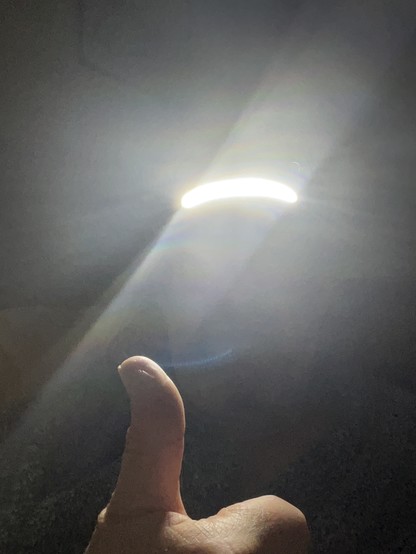 person wearing an LED head torch giving thumbs up. thumb illuminated but face not visible due to glare from LED light